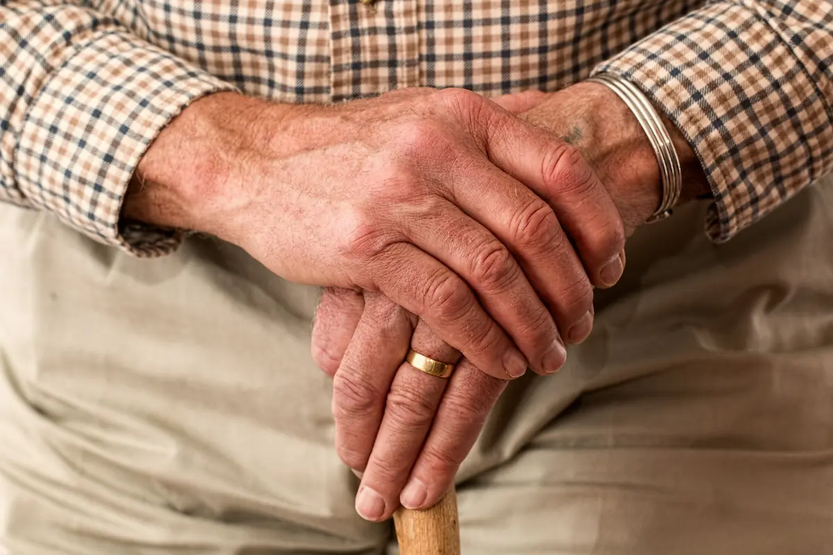 An older person’s hands resting on a walking stick