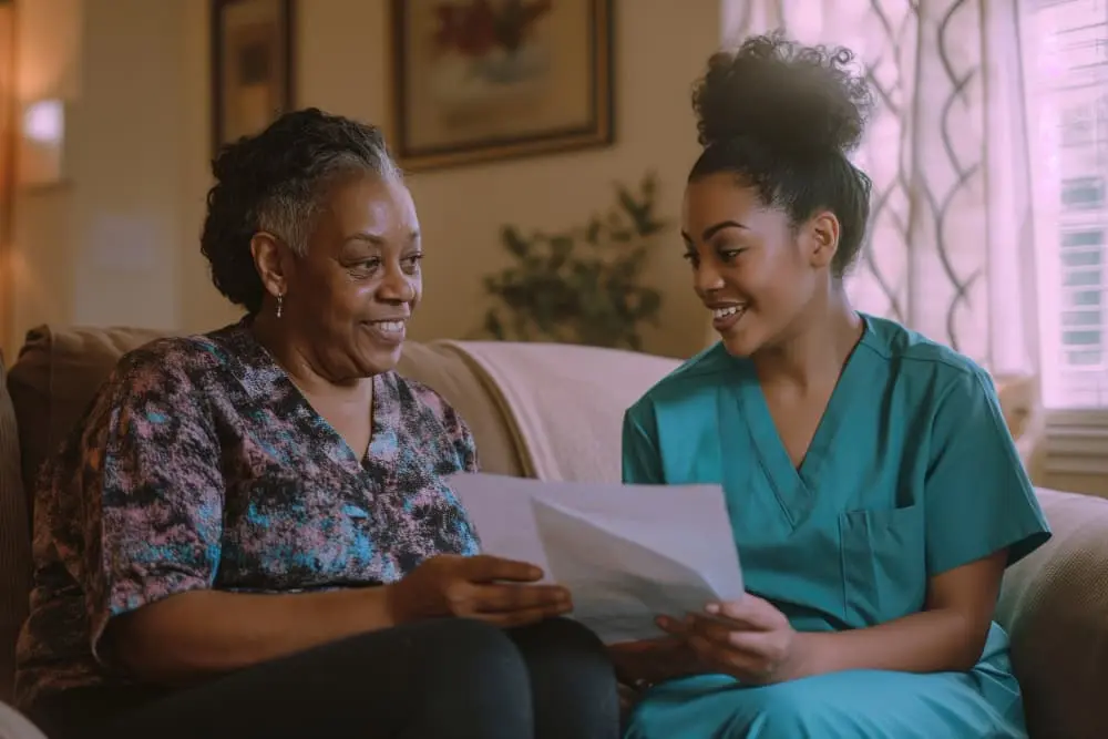 A caregiver going through paperwork with an older woman on her sofa